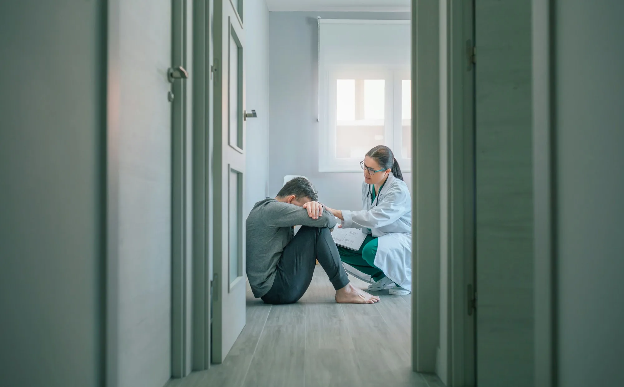 Doctor reassuring and helping to patient sitting on room floor