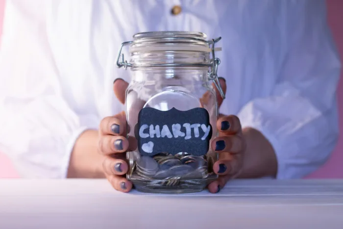Woman hands holding a glass jar with coins with a chalk Charity tag. Donation and charity concept